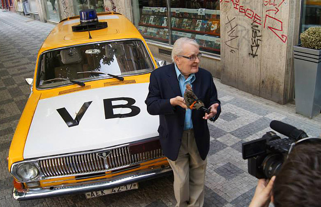 Herec Vladimír Brabec pózuje se sběratelskou figurkou majora Zemana před sovětskou Volhou v barvách Veřejné bezpečnosti